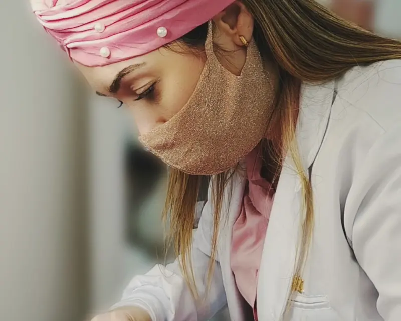 A Dra. Gabriela, de máscara e touca rosa, durante um procedimento facial